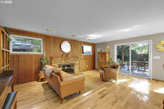 living room with light wood-style floors, plenty of natural light, a fireplace, and wooden walls