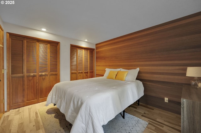 bedroom with wooden walls, recessed lighting, two closets, and light wood-style floors