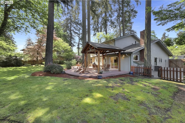 back of property featuring fence, a deck, a chimney, a gazebo, and a yard