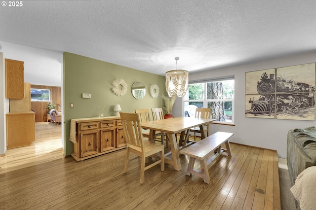dining area with an inviting chandelier, a textured ceiling, and light wood-style floors