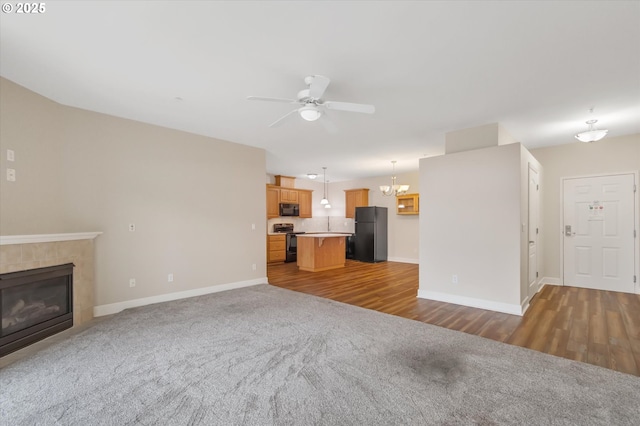 unfurnished living room featuring a tile fireplace, carpet floors, and ceiling fan with notable chandelier