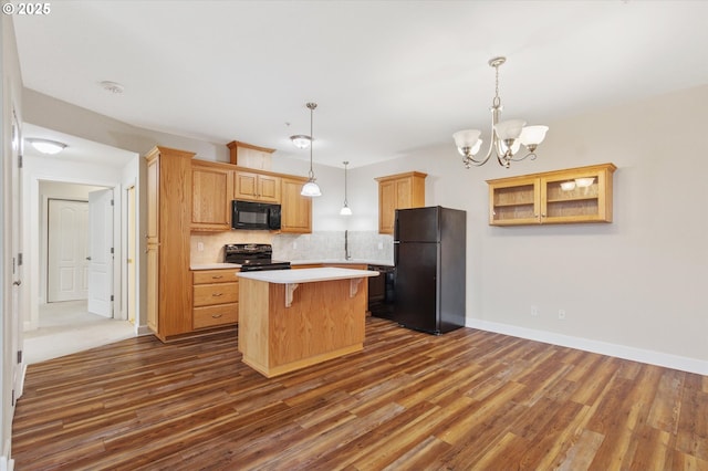 kitchen with an inviting chandelier, black appliances, decorative backsplash, a kitchen island, and a breakfast bar area