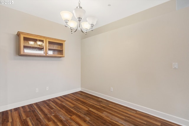 spare room featuring dark hardwood / wood-style flooring and a chandelier