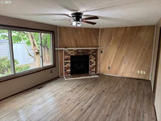 18622 SE Stephens Cir, Portland, OR 97233 - unfurnished living room with wooden walls, a ceiling fan, a textured ceiling, wood finished floors, and a brick fireplace