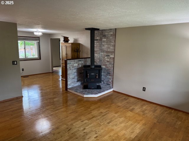 18622 SE Stephens Cir, Portland, OR 97233 - unfurnished living room featuring light wood-style floors, a wood stove, and a textured ceiling