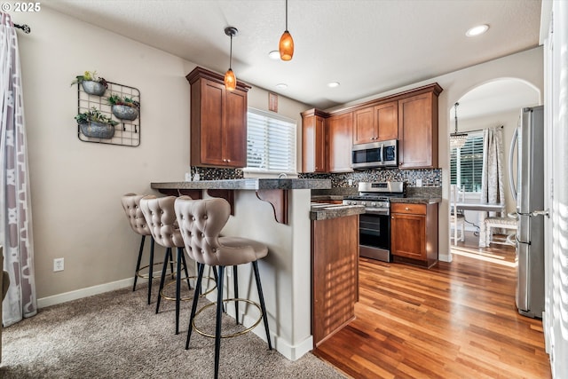 kitchen featuring a breakfast bar area, tasteful backsplash, decorative light fixtures, kitchen peninsula, and stainless steel appliances