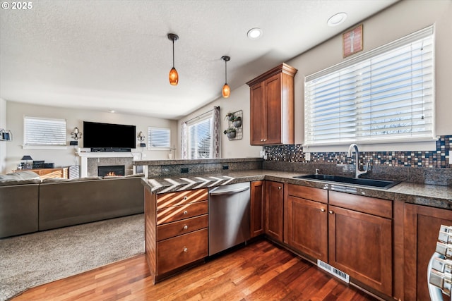 kitchen with sink, decorative light fixtures, dishwasher, a tile fireplace, and decorative backsplash