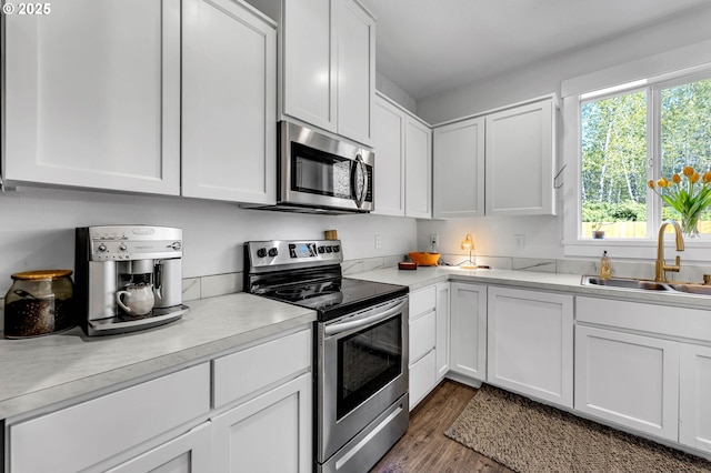 kitchen with stainless steel appliances, a sink, dark wood finished floors, white cabinetry, and light countertops