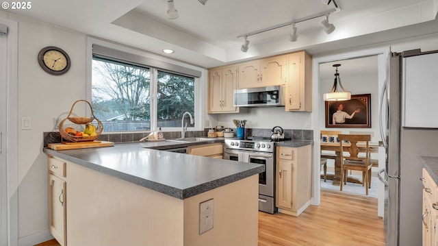 kitchen featuring light wood finished floors, stainless steel appliances, dark countertops, a sink, and a peninsula