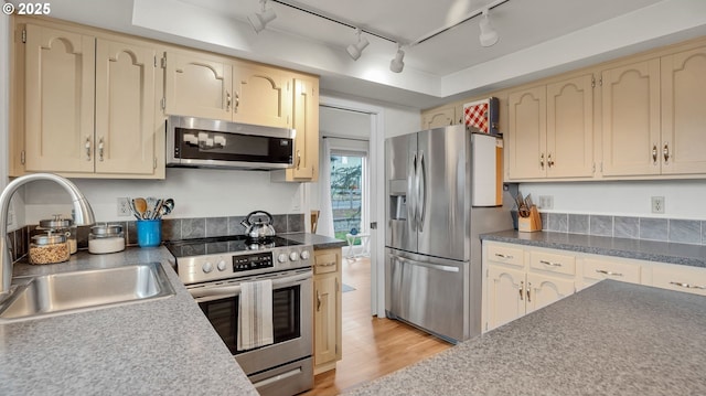 kitchen with dark countertops, cream cabinets, appliances with stainless steel finishes, a sink, and light wood-type flooring