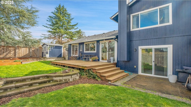 back of house featuring a deck, an outdoor structure, fence, a lawn, and a shed