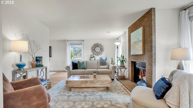 living room with a brick fireplace, a textured ceiling, and wood finished floors