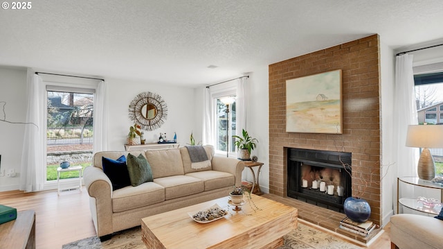 living room with a brick fireplace, light wood-style flooring, and a textured ceiling