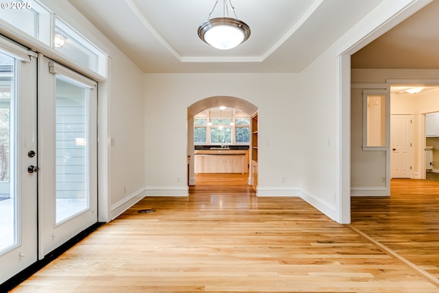 unfurnished dining area featuring a raised ceiling, sink, and light hardwood / wood-style flooring