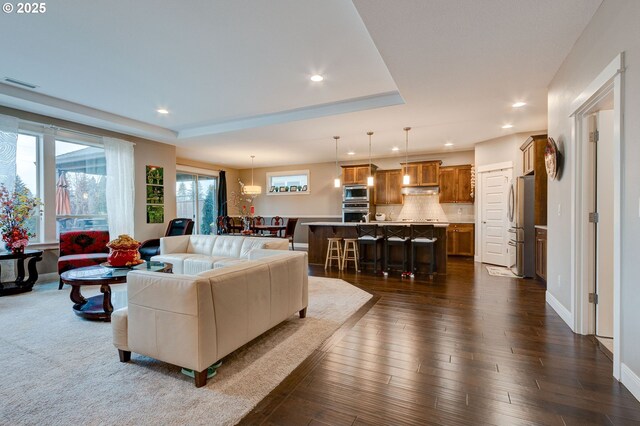 living room featuring plenty of natural light, dark wood-type flooring, and a tray ceiling