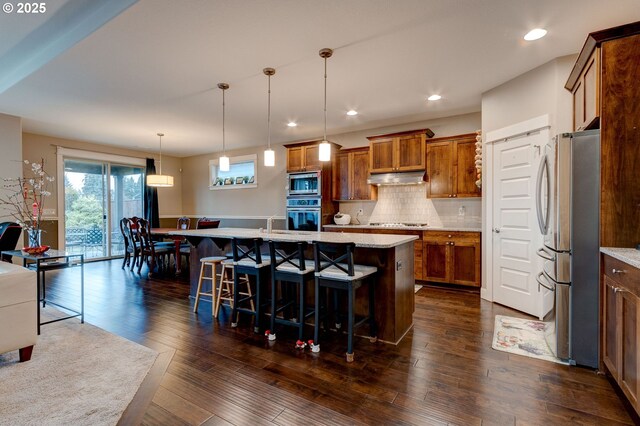 kitchen featuring decorative light fixtures, appliances with stainless steel finishes, dark hardwood / wood-style floors, a kitchen breakfast bar, and an island with sink