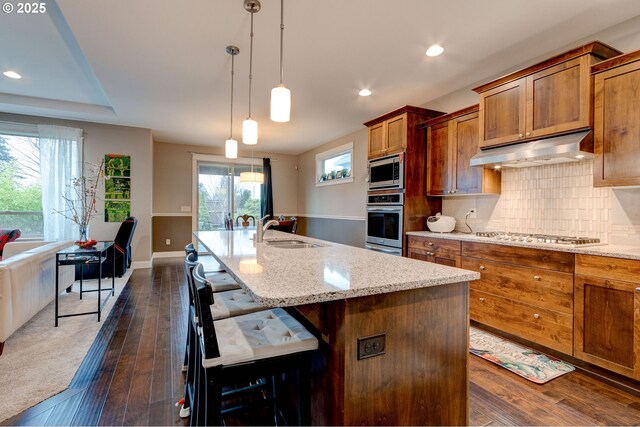 kitchen with sink, a kitchen breakfast bar, stainless steel appliances, a kitchen island with sink, and backsplash