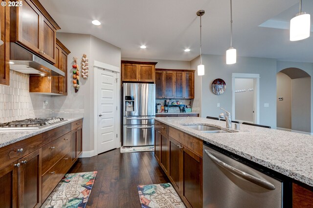 kitchen featuring stainless steel appliances, hanging light fixtures, sink, and light stone counters