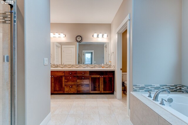 bathroom featuring tile patterned flooring, vanity, tiled bath, and toilet