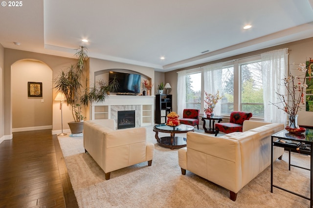 living room featuring hardwood / wood-style flooring, a tile fireplace, and a raised ceiling