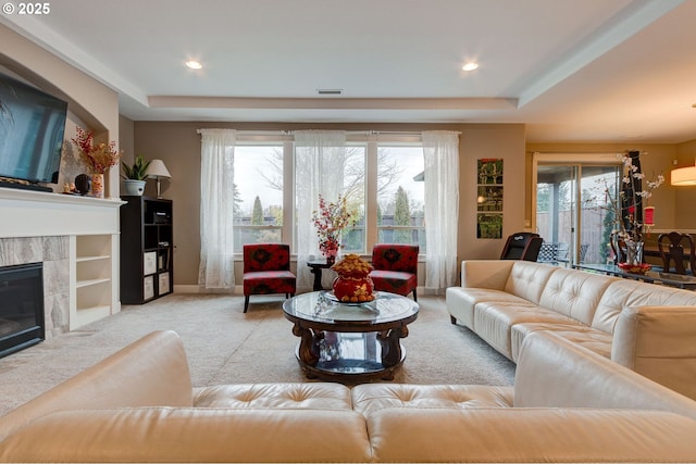 living room featuring a tray ceiling, a tile fireplace, and light colored carpet