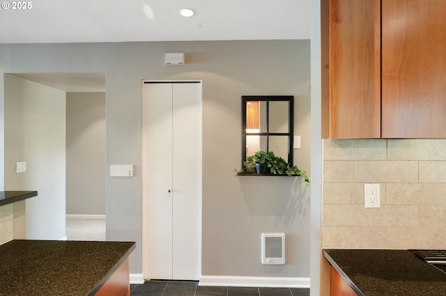 kitchen featuring dark stone counters, decorative backsplash, baseboards, brown cabinets, and dark tile patterned floors