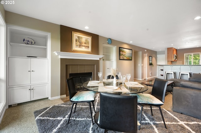 dining room featuring a tiled fireplace, built in shelves, baseboards, and recessed lighting