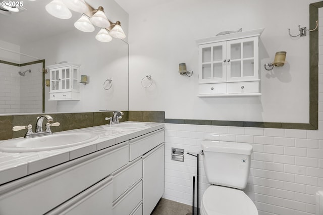 full bathroom featuring toilet, tile walls, wainscoting, double vanity, and a shower
