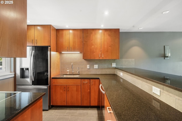 kitchen featuring stainless steel appliances, a sink, brown cabinets, dark stone countertops, and decorative backsplash