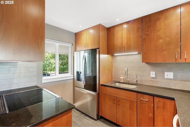 kitchen featuring stainless steel fridge with ice dispenser, a sink, brown cabinets, dark stone counters, and range