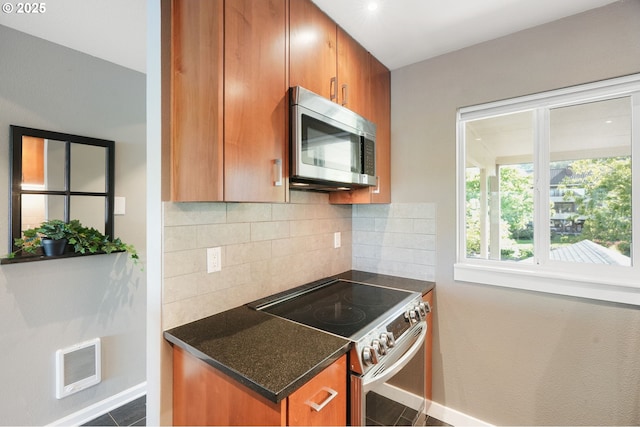 kitchen with appliances with stainless steel finishes, decorative backsplash, brown cabinets, and baseboards
