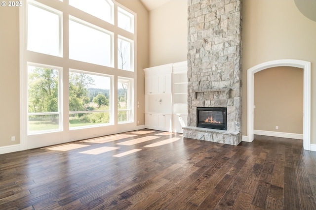 unfurnished living room featuring dark wood-type flooring, a stone fireplace, and a high ceiling