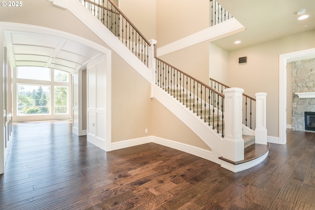 staircase with a stone fireplace, hardwood / wood-style floors, and a high ceiling