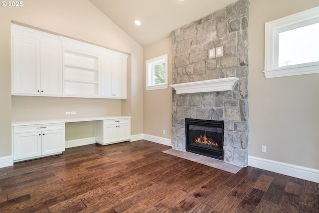 unfurnished office with lofted ceiling, dark hardwood / wood-style flooring, built in desk, and a fireplace