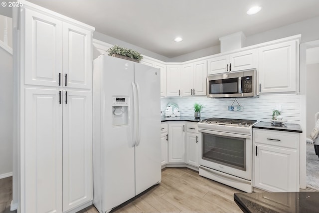 kitchen featuring dark countertops, white appliances, white cabinetry, and light wood finished floors