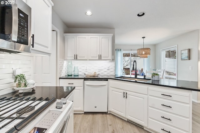 kitchen featuring light wood finished floors, stainless steel microwave, white dishwasher, white cabinetry, and a sink