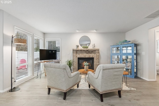 living room featuring light wood-type flooring, a brick fireplace, visible vents, and baseboards