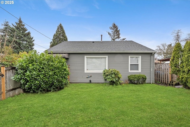 back of house featuring a shingled roof, a fenced backyard, and a yard