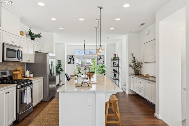 kitchen with stainless steel appliances, a kitchen island with sink, decorative backsplash, a kitchen bar, and recessed lighting