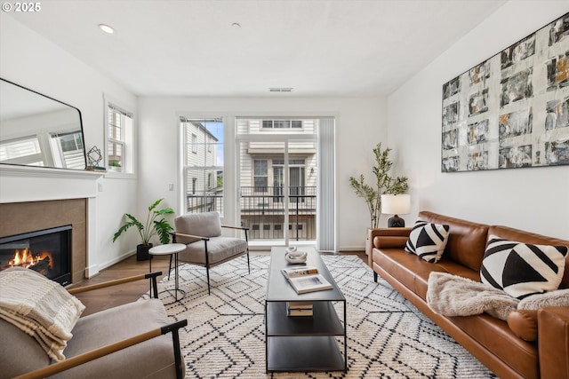 living area with wood finished floors, a tiled fireplace, baseboards, and recessed lighting