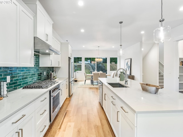 kitchen with an island with sink, appliances with stainless steel finishes, sink, and pendant lighting