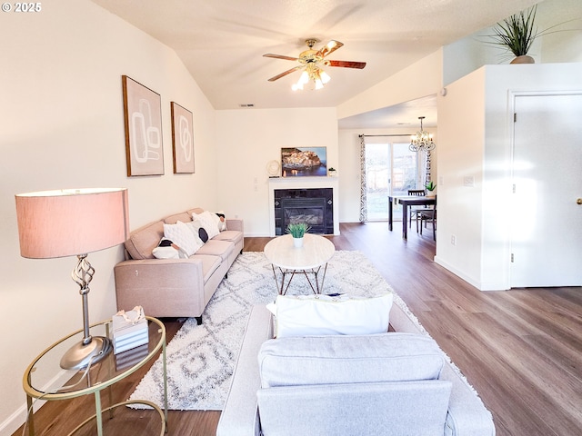 living room with a tile fireplace, lofted ceiling, hardwood / wood-style floors, and ceiling fan with notable chandelier