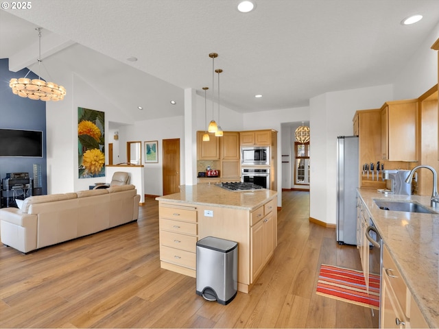 kitchen featuring light brown cabinets, open floor plan, a sink, light wood finished floors, and appliances with stainless steel finishes