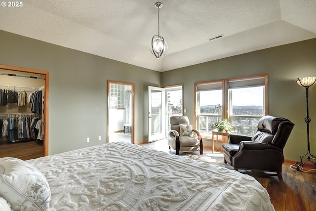 bedroom with wood finished floors, visible vents, lofted ceiling, a textured ceiling, and a walk in closet