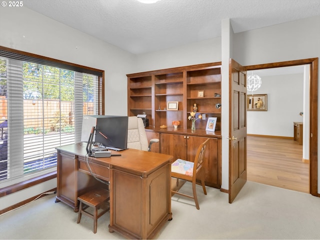 office area featuring baseboards, a textured ceiling, and light carpet