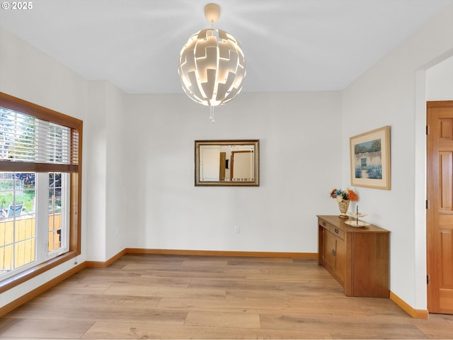 spare room featuring an inviting chandelier, baseboards, and light wood-style floors