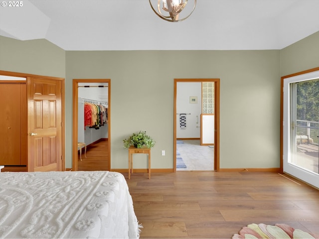 bedroom with light wood-style floors, a walk in closet, lofted ceiling, and a chandelier