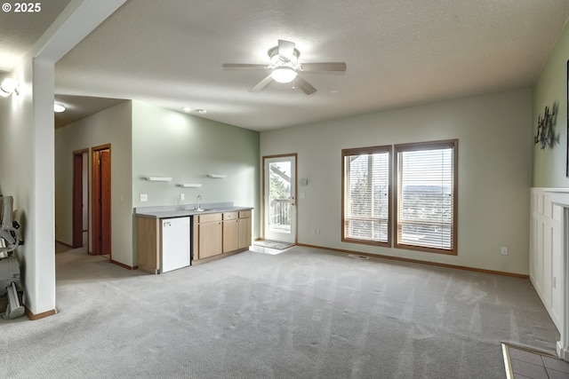 unfurnished living room featuring a textured ceiling, light carpet, a ceiling fan, and a sink