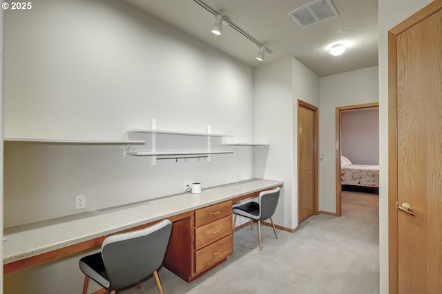 home office featuring visible vents, rail lighting, baseboards, light colored carpet, and built in study area