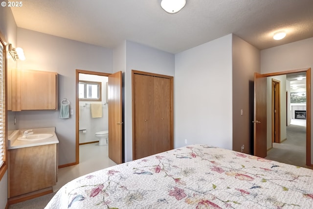 bedroom with ensuite bath, a closet, a glass covered fireplace, a textured ceiling, and a sink